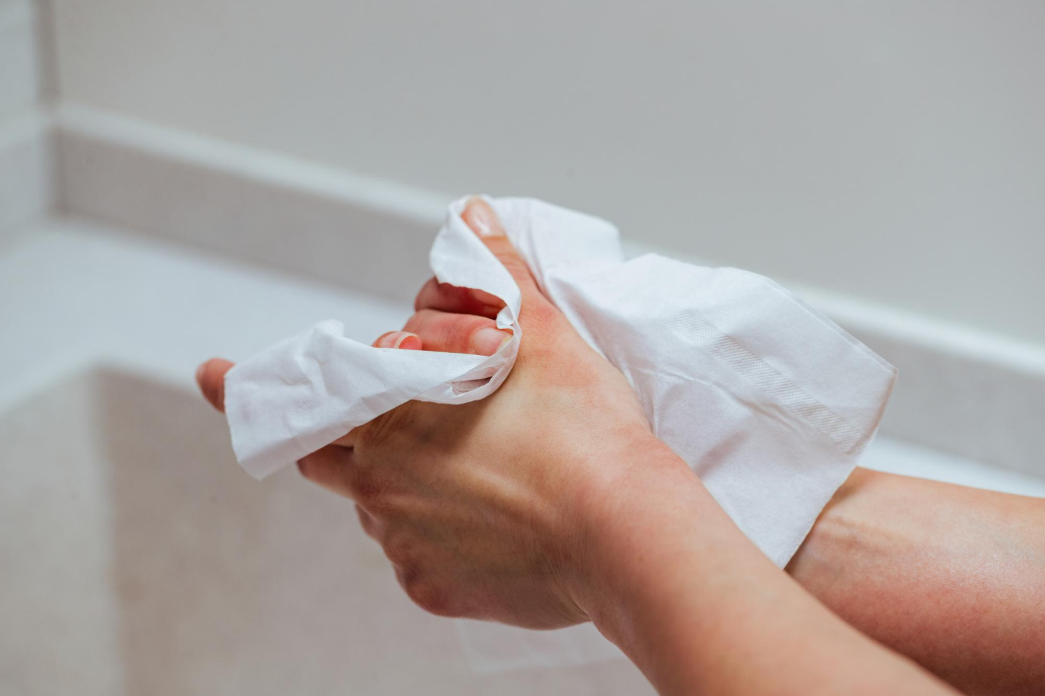 Two hands are drying with a white paper towel in a bathroom. The setting is clean and minimalistic, conveying a sense of hygiene and routine.